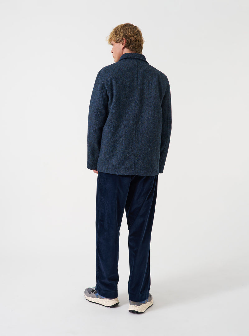 A model wearing the Blue/Black Harris Tweed OG Bakers Chore Jacket, viewed from behind against a plain background. The image displays the relaxed fit, straight hem, and back panel of the dark tweed jacket.