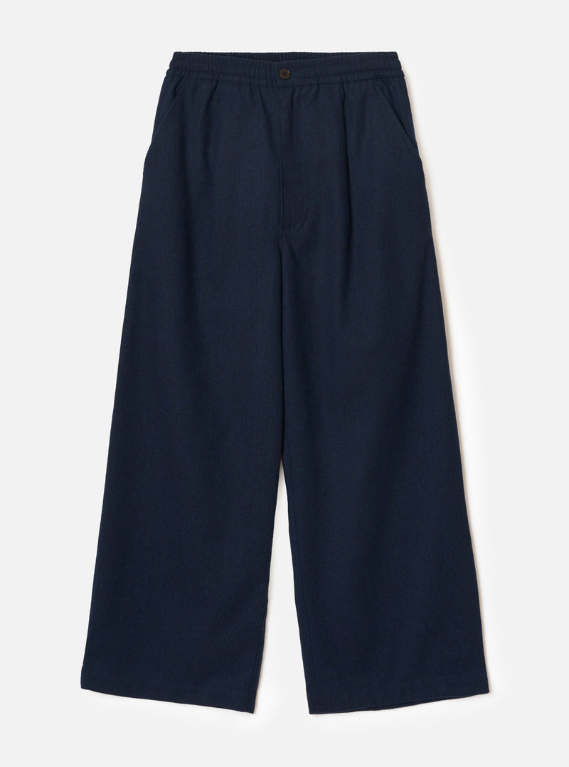 Navy wool herringbone wide-leg trousers laid flat on a plain light grey backdrop. The elasticated waistband features a single dark metal button at the centre front. Two side slash pockets sit at the hips. The fabric has a subtle herringbone texture throughout. Full-length legs with a wide, relaxed silhouette and plain hem.