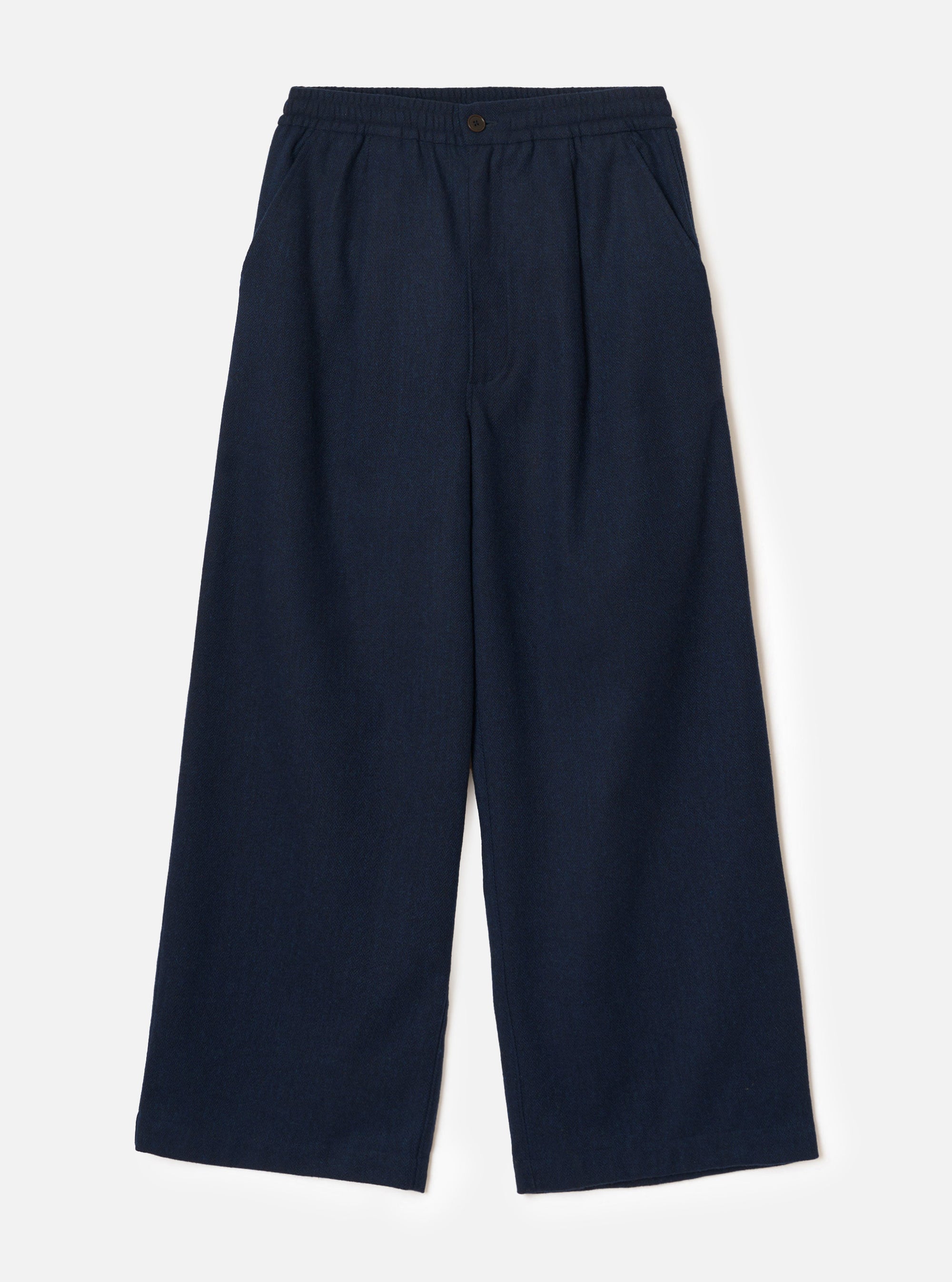Navy wool herringbone wide-leg trousers laid flat on a plain light grey backdrop. The elasticated waistband features a single dark metal button at the centre front. Two side slash pockets sit at the hips. The fabric has a subtle herringbone texture throughout. Full-length legs with a wide, relaxed silhouette and plain hem.