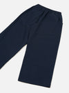 Navy wool herringbone trousers laid flat on a light grey surface, shot at an angle. A fully elasticated waistband sits at the top with visible gather. The wide leg tapers slightly to a plain unfinished hem. A side pocket opening is visible on the right. The plain-weave fabric shows a subtle texture across the surface.