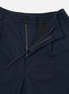 Close-up flat lay of navy wool herringbone trousers on a white studio backdrop. The waistband features an elasticated back and a navy drawcord. The fly is open, showing a brass zip and a single dark horn button above. A black lining is visible beneath the open fly flap.