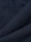 Close-up of navy wool herringbone fabric, showing the diagonal zigzag weave pattern in deep navy and dark charcoal tones with subtle blue flecks. The cloth is folded to highlight its texture and weight. No garment construction details are visible.