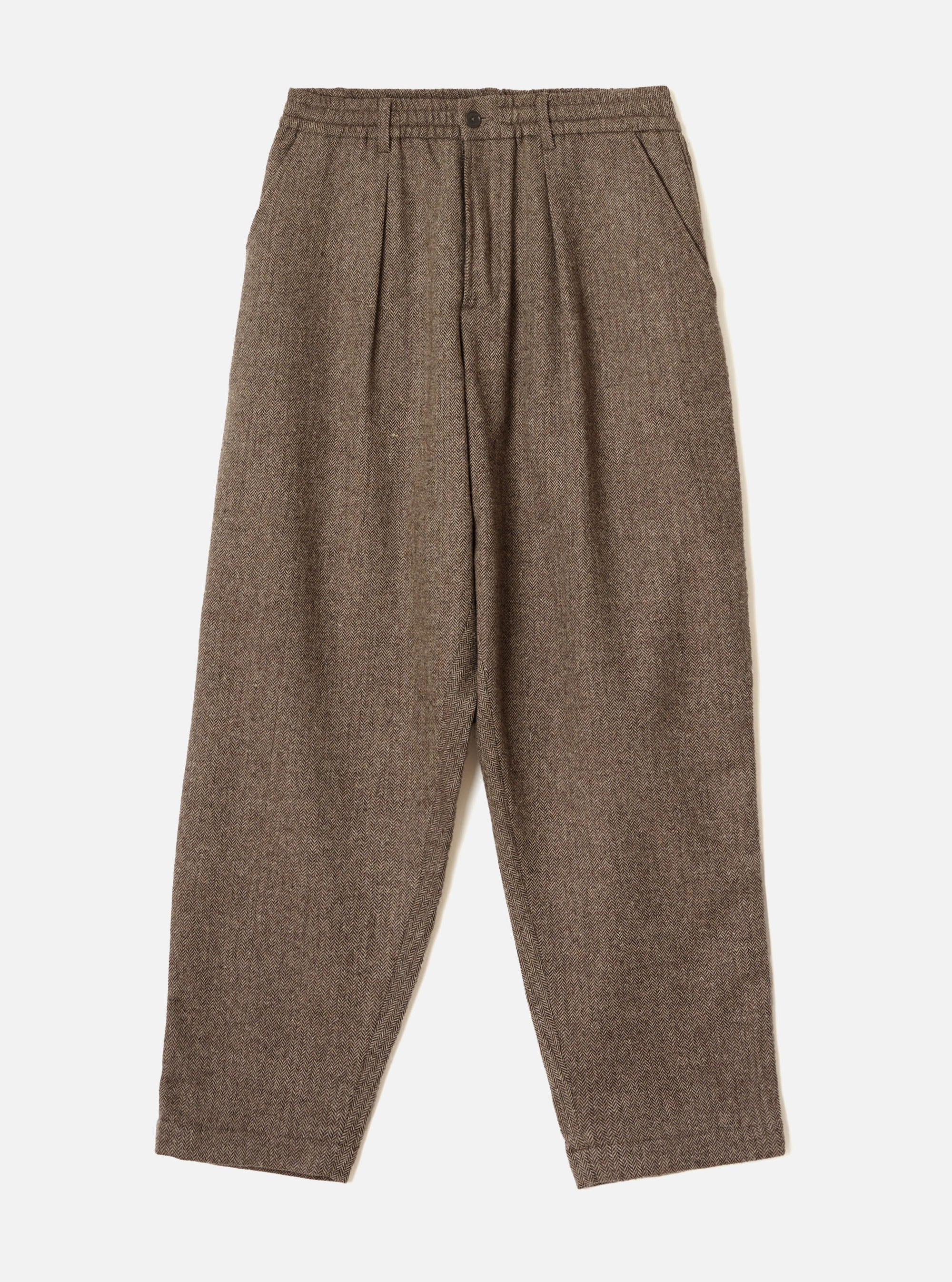 Brown wool herringbone pleated trousers laid flat on a light grey studio backdrop. The fabric shows a fine herringbone weave throughout. A structured waistband features a single button fastening and slanted side pockets. Double pleats run from the waistband to full-length tapered legs with plain hems.