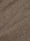 Close-up detail shot of brown wool herringbone fabric. The tightly woven chevron pattern is visible in dark brown and ecru tones across folded and creased sections of the trouser cloth, showing the texture and weight of the material.