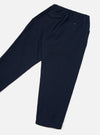 Navy wool herringbone track pants laid flat on a light grey surface, showing the back. An elasticated waistband sits at the top with two button-fastened welt pockets visible. The fabric has a fine herringbone texture. The tapered leg narrows toward the plain, unfinished hem.