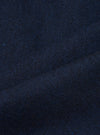 Close-up of navy wool herringbone fabric, showing the diagonal zigzag weave pattern in deep navy and dark charcoal tones with flecks of bright blue. The cloth is gathered and folded, highlighting the texture and weight of the woven wool.