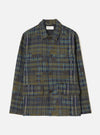 Olive shadows check chore jacket in a woven plaid of olive, navy and blue tones with a distressed check texture. Point collar, four-button placket with dark brown buttons, chest patch pocket and two large flap patch pockets at the hem. Universal Works woven label at the neck. Flat lay on a light grey studio backdrop.