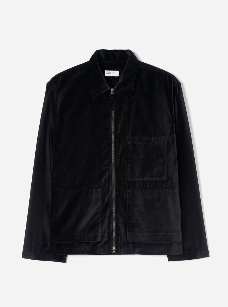 Black velvet zip-through overshirt on a plain light grey studio backdrop. Features a point collar, full-length black zip with silver metal pull tabs at top and bottom, one chest patch pocket, two lower patch pockets, and long plain sleeves. A woven Universal Works label sits inside the collar.