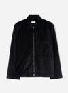 Black velvet zip-through overshirt on a plain light grey studio backdrop. Features a point collar, full-length black zip with silver metal pull tabs at top and bottom, one chest patch pocket, two lower patch pockets, and long plain sleeves. A woven Universal Works label sits inside the collar.