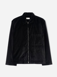 Black velvet zip-through overshirt on a plain light grey studio backdrop. Features a point collar, full-length black zip with silver metal pull tabs at top and bottom, one chest patch pocket, two lower patch pockets, and long plain sleeves. A woven Universal Works label sits inside the collar.