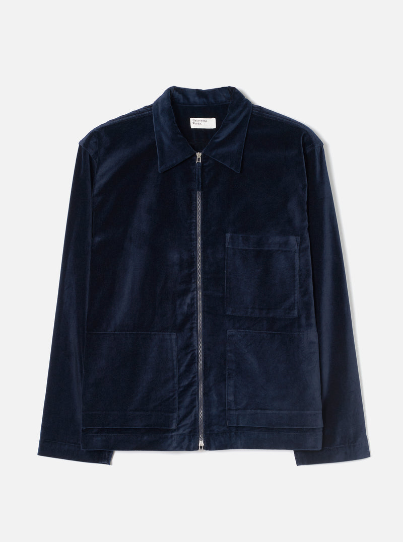 Navy velvet overshirt laid flat on a light grey seamless backdrop. Full-length silver zip runs from hem to a point collar. One chest patch pocket sits on the right, two larger patch pockets at the hip. Long sleeves with plain cuffs. Small woven Universal Works label visible inside the collar.