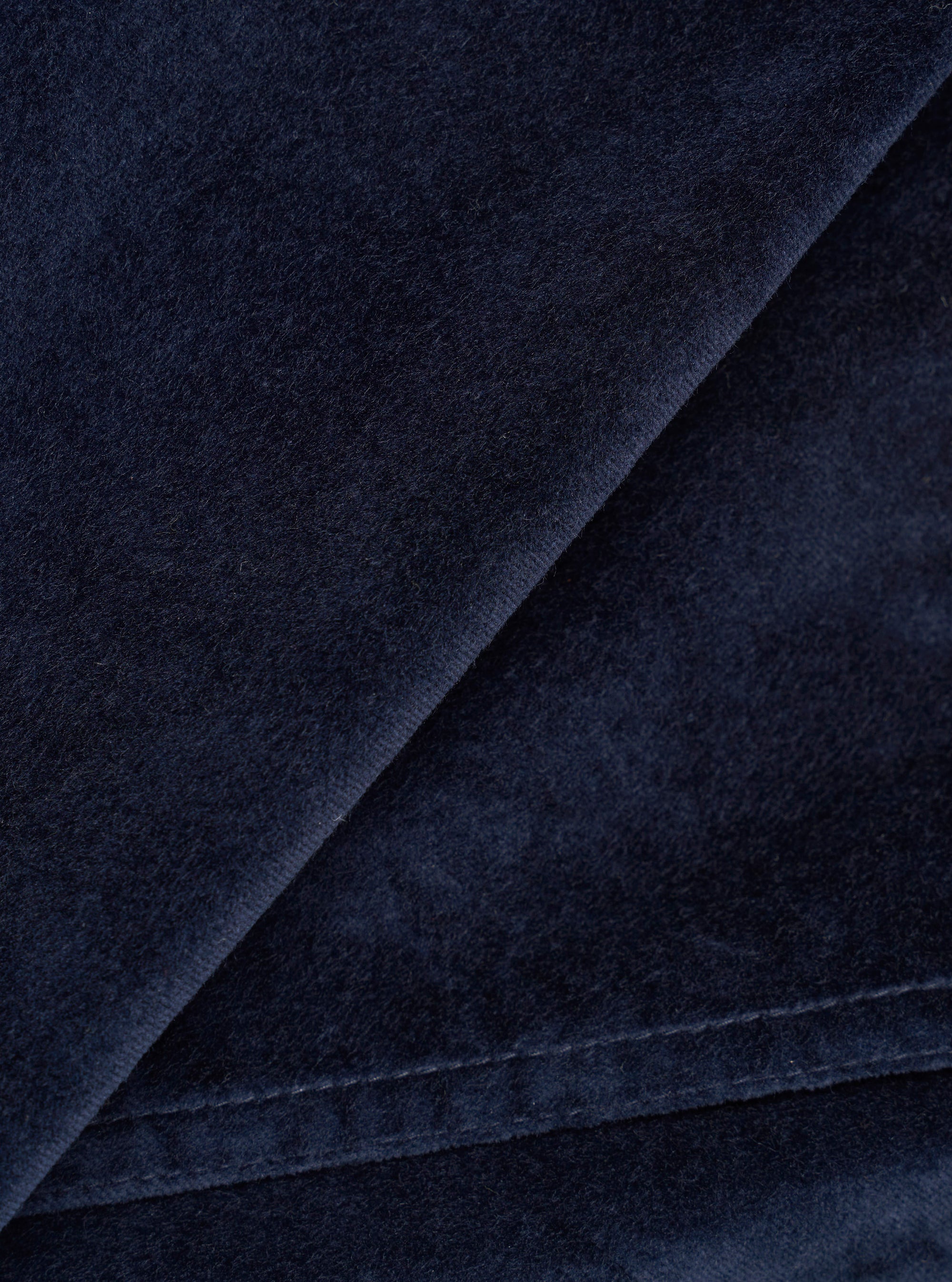 Close-up detail of the navy velvet fabric used in the CPH Zip OS Shirt. The shot highlights the dense, soft pile of the velvet with a folded edge running diagonally across the frame, revealing the fabric's depth and slight sheen against a dark navy ground.