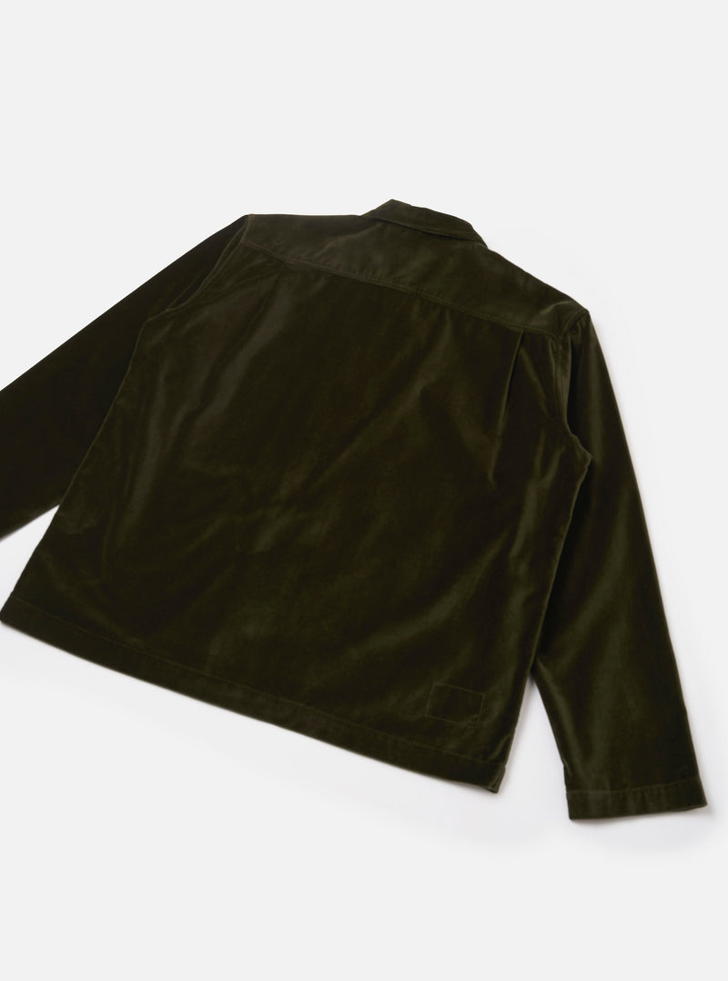Back view of an olive velvet zip shirt, laid flat on a light grey surface. The smooth, lustrous velvet fabric shows light-catching sheen across the back panel and long sleeves. A rear yoke seam runs across the upper back, and a small welt pocket sits at the lower right. The cuffs are plain with no visible buttons.