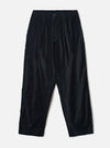 Black velvet Oxford trousers laid flat on a light grey seamless backdrop. The wide-leg, tapered silhouette features a double-pleated front, elasticated waistband with a single button fastening, and side seam pockets. The fine-wale velvet fabric has a subtle sheen. Hem is plain and unfinished at the ankle.