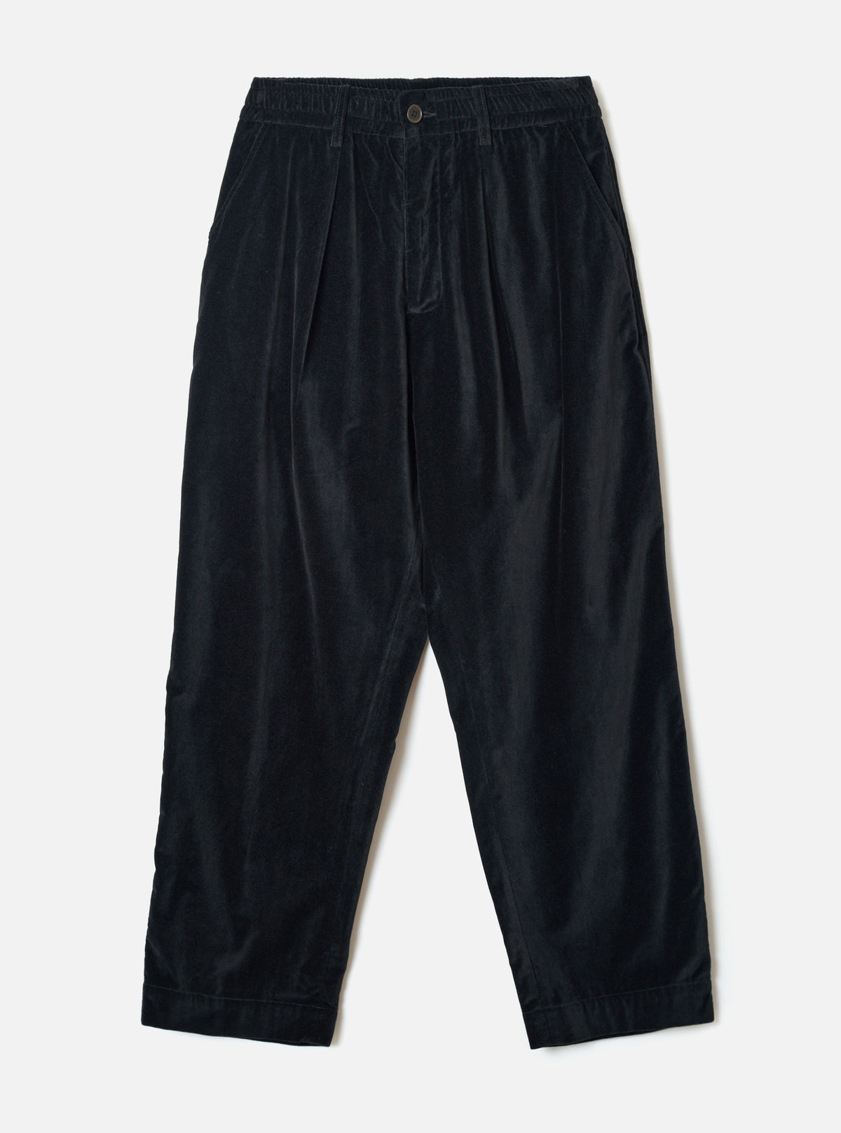 Black velvet Oxford trousers laid flat on a light grey seamless backdrop. The wide-leg, tapered silhouette features a double-pleated front, elasticated waistband with a single button fastening, and side seam pockets. The fine-wale velvet fabric has a subtle sheen. Hem is plain and unfinished at the ankle.
