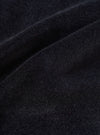 Close-up detail shot of the black velvet fabric used in the CPH Oxford Pant. The surface shows a dense, soft pile with a fine brushed texture and subtle dark navy undertones. Occasional flecks of red and orange fibre are visible throughout. The fabric is folded, highlighting its weight and drape.