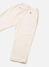 Ecru velvet Oxford trousers laid flat on a light grey seamless backdrop. The elasticated waistband features a small metal eyelet detail at the front. Fine velvet texture is visible across the fabric. Side seams run the full length of the leg to the plain hem.