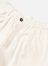 Close-up of ecru velvet Oxford trousers against a light grey studio backdrop. The ribbed elastic waistband is shown in detail alongside a single dark horn button at the fly. A slash pocket is visible to the left. The smooth velvet fabric has a soft, matte texture.