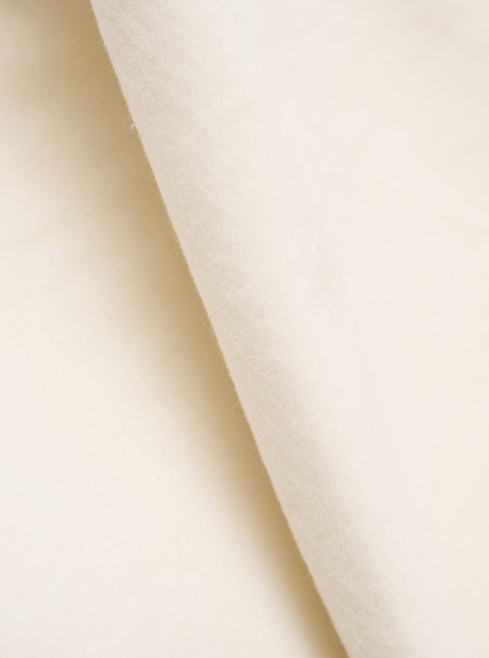 Close-up detail shot of the ecru velvet fabric used in the CPH Velvet Oxford Pant. The soft, dense pile is visible across the folded edge, showing the plush texture and subtle nap of the cream-toned velvet against a plain white studio backdrop.