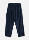 Navy velvet Oxford trousers laid flat on a light grey studio backdrop. Fine-wale velvet fabric with a subtle sheen. Elasticated waistband with a single centre button, double forward pleats, side slash pockets, and tapered legs with plain hems.