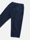 Navy velvet Oxford trousers laid flat on a light grey surface, shot from above at an angle. Fine-wale velvet texture is visible across the fabric. The elasticated waistband is shown at the top, with a buttoned welt pocket on the back and a side pocket visible. The tapered legs end in plain hems.