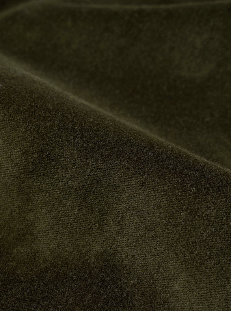 Close-up detail of the olive velvet fabric used in the Oxford pant. Fine ribbed texture and soft pile are visible, with gentle folds showing the depth and sheen of the velvet. The dark olive tone shifts subtly where the fabric creases.
