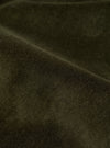 Close-up detail of the olive velvet fabric used in the Oxford pant. Fine ribbed texture and soft pile are visible, with gentle folds showing the depth and sheen of the velvet. The dark olive tone shifts subtly where the fabric creases.