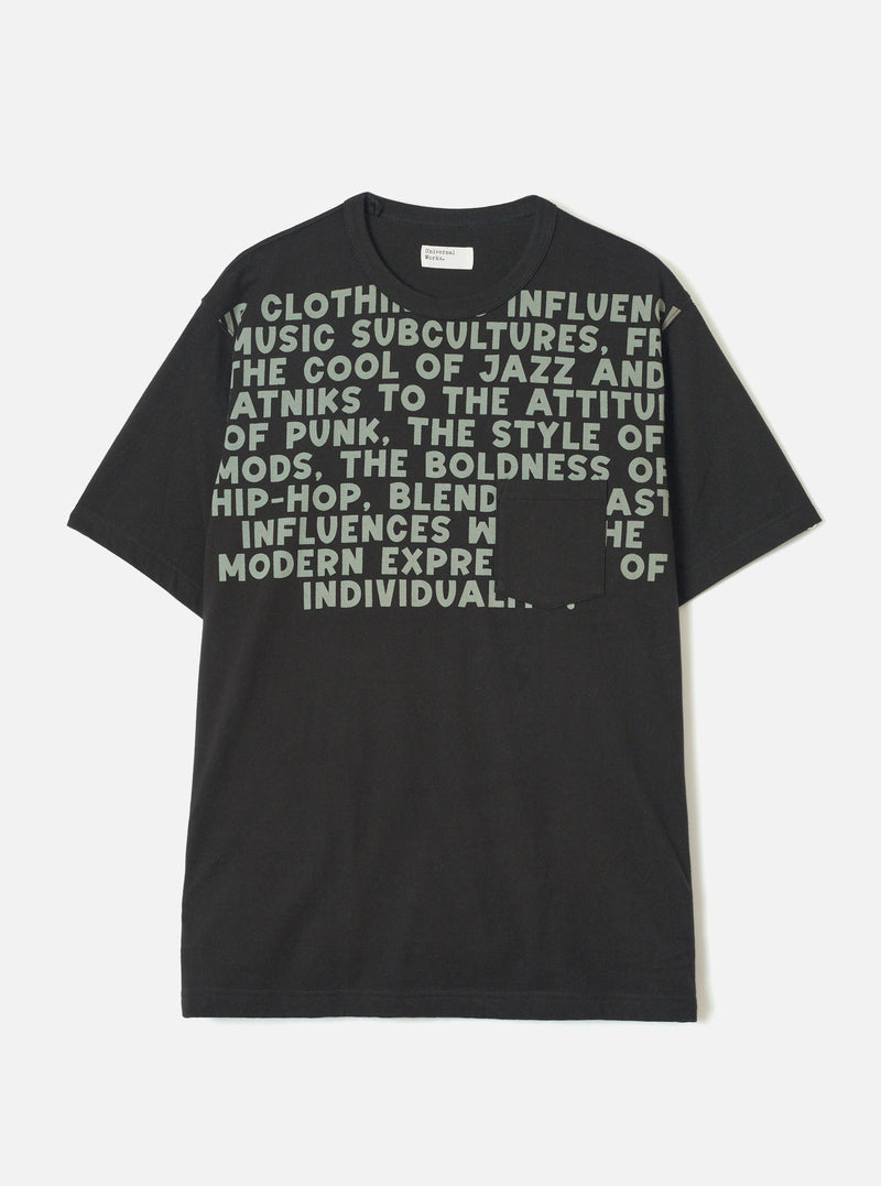 Black short-sleeve t-shirt in single jersey cotton, laid flat on a light grey studio backdrop. Crew neck with a small woven Universal Works label at the back neck. Large sage green bold text print covers the chest, referencing jazz, punk, mods and hip-hop. A plain patch pocket sits at the lower right chest, partially obscuring the print.