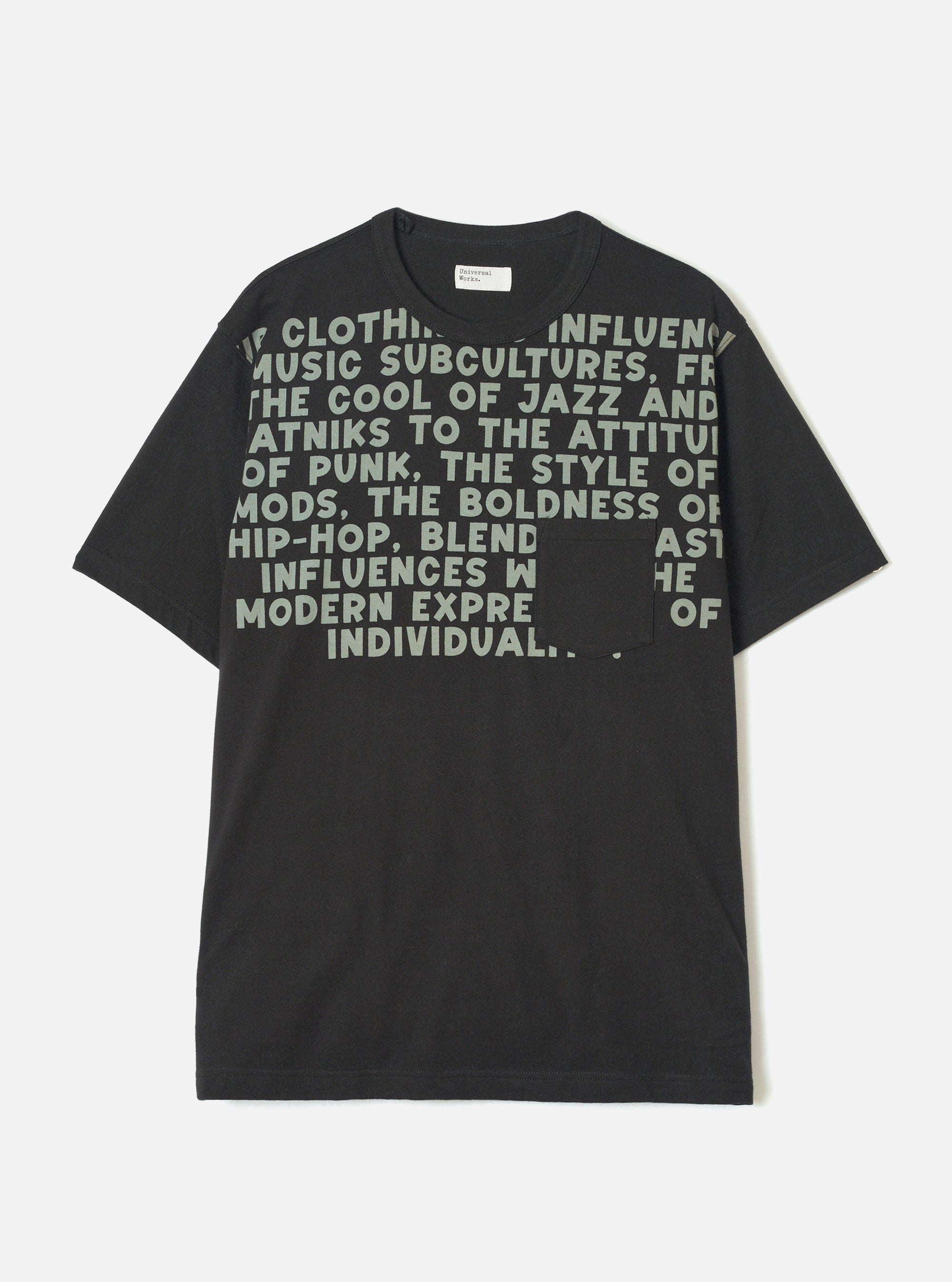Black short-sleeve t-shirt in single jersey cotton, laid flat on a light grey studio backdrop. Crew neck with a small woven Universal Works label at the back neck. Large sage green bold text print covers the chest, referencing jazz, punk, mods and hip-hop. A plain patch pocket sits at the lower right chest, partially obscuring the print.