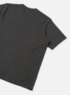 Back view of a black single jersey pocket tee, laid flat on a light grey surface. The shot is cropped to show the upper back, one short sleeve with a plain hem, and a care label visible at the nape of the neck. The fabric is smooth with a fine jersey knit texture.