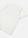 Flat lay of an ecru single jersey pocket tee on a white surface, shot from a diagonal angle showing the back and one short sleeve. The plain jersey fabric has a soft, lightweight texture with natural drape. A ribbed short sleeve cuff is visible on the right side.