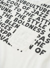 Close-up flat lay of an ecru single jersey pocket tee. The front is covered in an all-over black text print featuring phrases including "subculture", "cool of jazz" and "boldness". A plain chest patch pocket in matching ecru sits centre-left. The crew neckline is visible at the top edge.