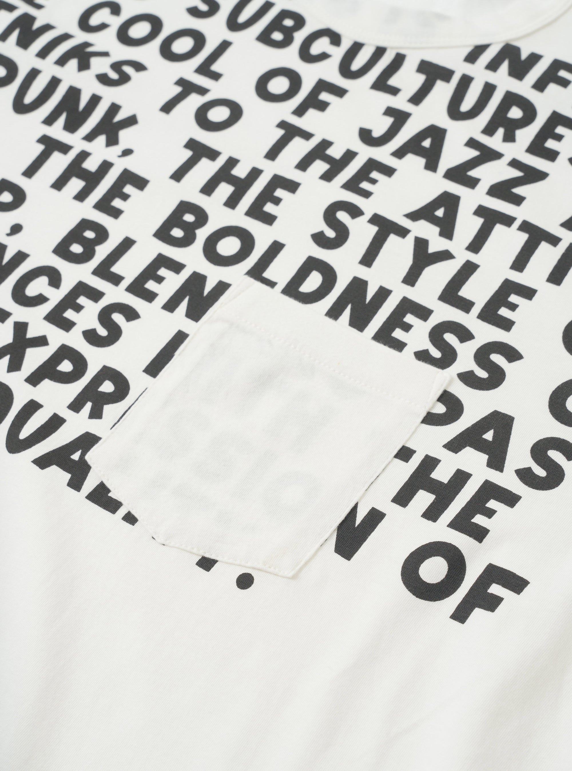 Close-up flat lay of an ecru single jersey pocket tee. The front is covered in an all-over black text print featuring phrases including "subculture", "cool of jazz" and "boldness". A plain chest patch pocket in matching ecru sits centre-left. The crew neckline is visible at the top edge.