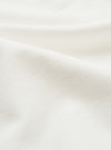 Close-up of the ecru single jersey fabric used in the Jazz Core Pocket Tee. The fine, smooth knit texture is visible across soft draped folds, showing a uniform diagonal weave structure in an off-white tone.