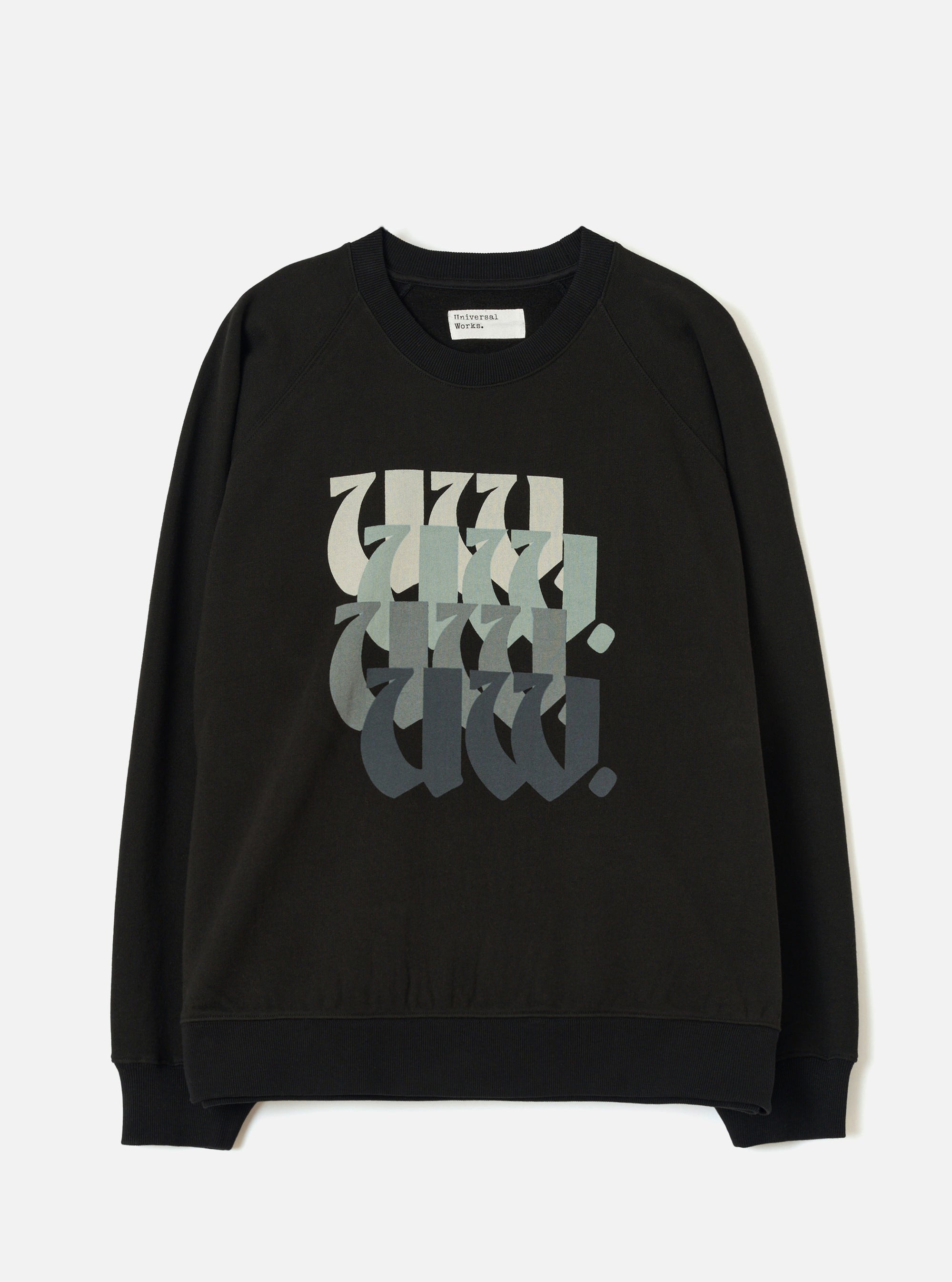 Black raglan sweatshirt laid flat on a light grey studio surface. Ribbed crew neck with a Universal Works woven label at the back neck. Ribbed cuffs and hem. Chest features a repeated "UW." graphic in blackletter style, fading from pale sage to dark charcoal across four stacked rows.