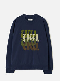 Navy brushback raglan sweatshirt laid flat on a light grey studio backdrop. Ribbed crew neck, ribbed cuffs and hem. A Universal Works label sits inside the collar. The chest features a stacked repeat "UW." graphic in blackletter script, graduating in colour from olive green through cream and dark green to brown.