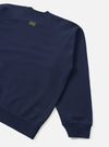 Navy brush back raglan sweatshirt, flat lay on a light grey seamless backdrop. Close-up of the back and left sleeve, showing the raglan seam, ribbed cuff and hem. A small olive green UW logo is printed at the centre back yoke. A stitched patch detail sits above the ribbed hem.