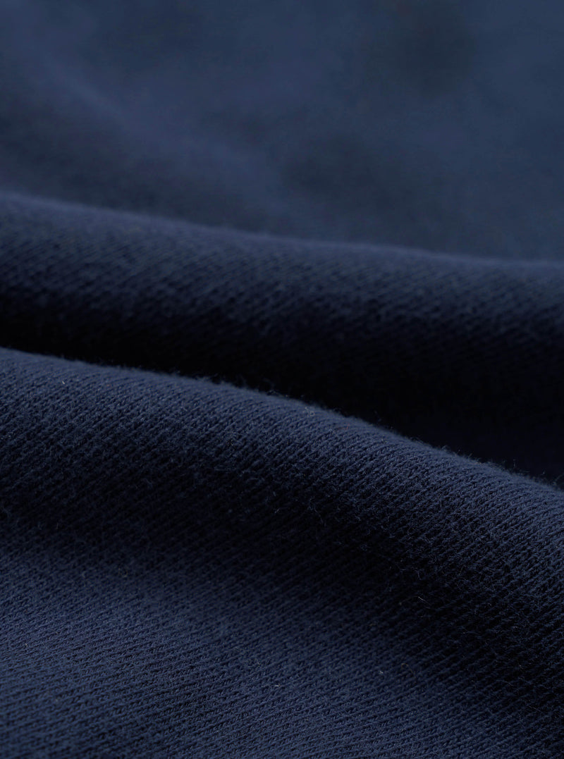 Close-up detail shot of navy brushback fleece fabric, showing a soft, dense looped texture on the reverse side and a smooth face. The material is folded to reveal both surfaces, highlighting the fabric's weight and finish.