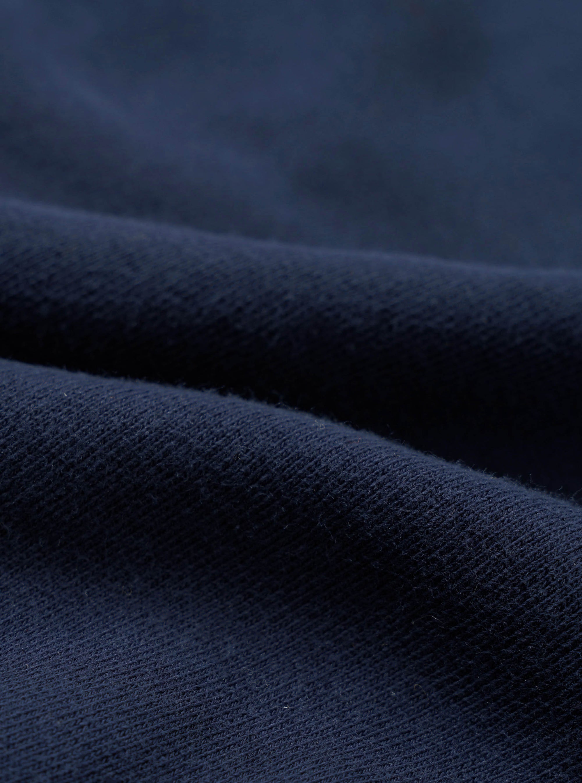 Close-up detail shot of navy brushback fleece fabric, showing a soft, dense looped texture on the reverse side and a smooth face. The material is folded to reveal both surfaces, highlighting the fabric's weight and finish.