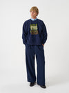 A front product view of the Universal Works Navy Brush Back Sweat UW UW Print Raglan Sweatshirt on a plain background. The navy blue cotton pullover features long raglan sleeves, a ribbed crew neck, ribbed hem, and front chest detail.