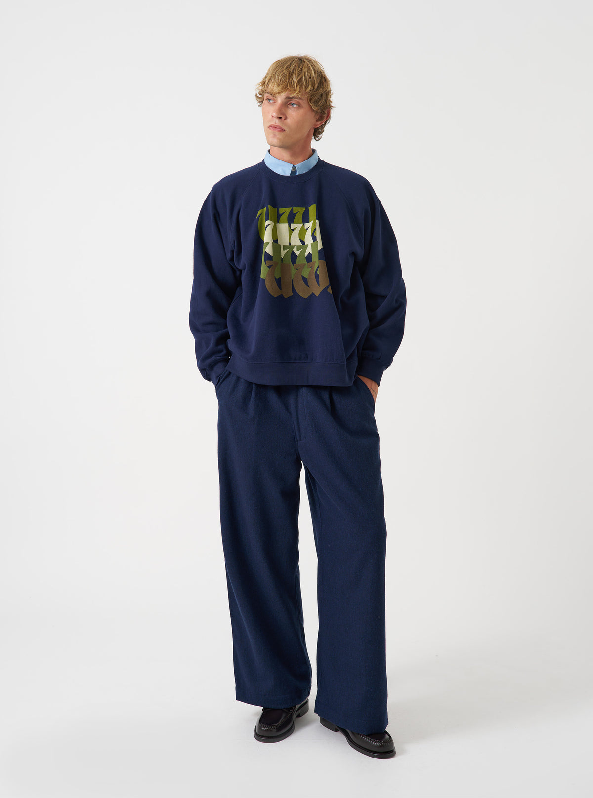 A model wearing the Universal Works Navy Brush Back Sweat UW UW Print Raglan Sweatshirt, captured from the front. The navy blue fleece-backed cotton sweatshirt displays raglan sleeves and a printed design against a plain backdrop.