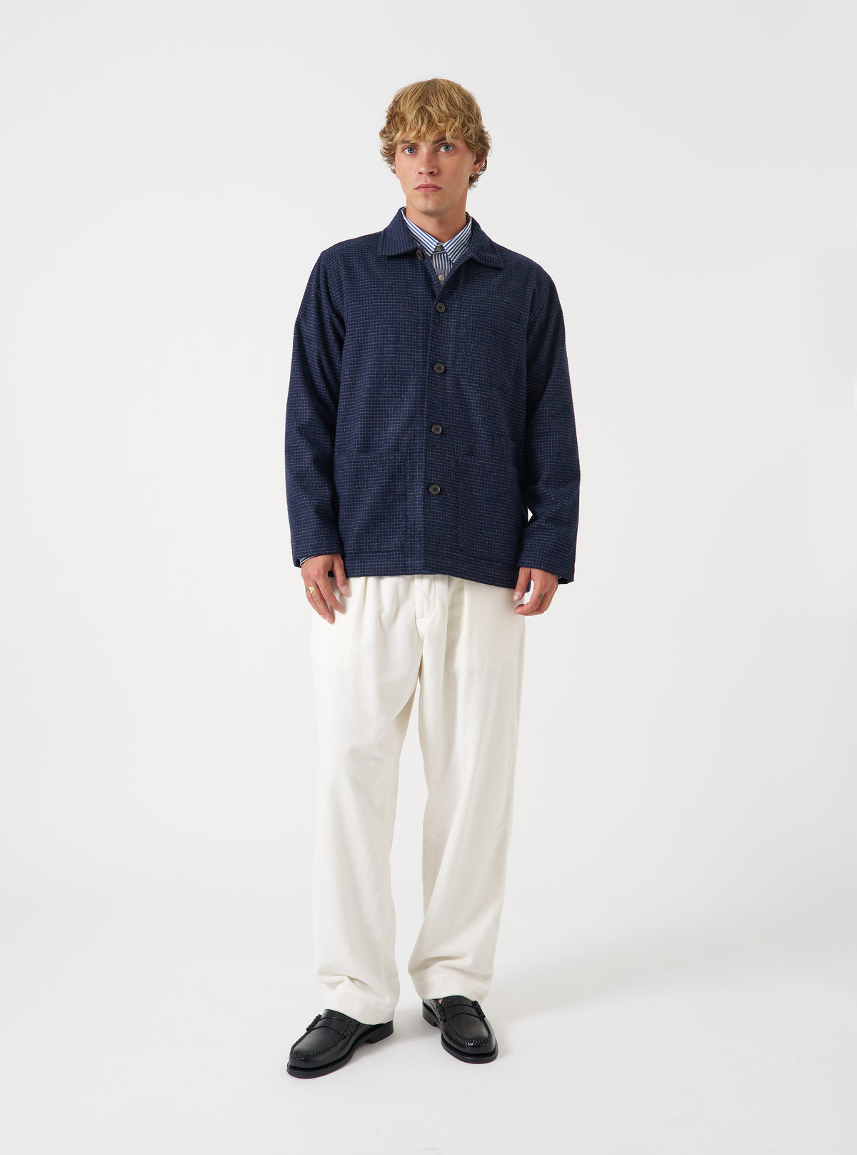 A front view of a model wearing the Universal Works Navy Check Bobby Wool Mix Bakers Overshirt. The dark blue check overshirt features a button front fastening, classic collar, chest pocket, and lower patch pockets against a plain neutral background.