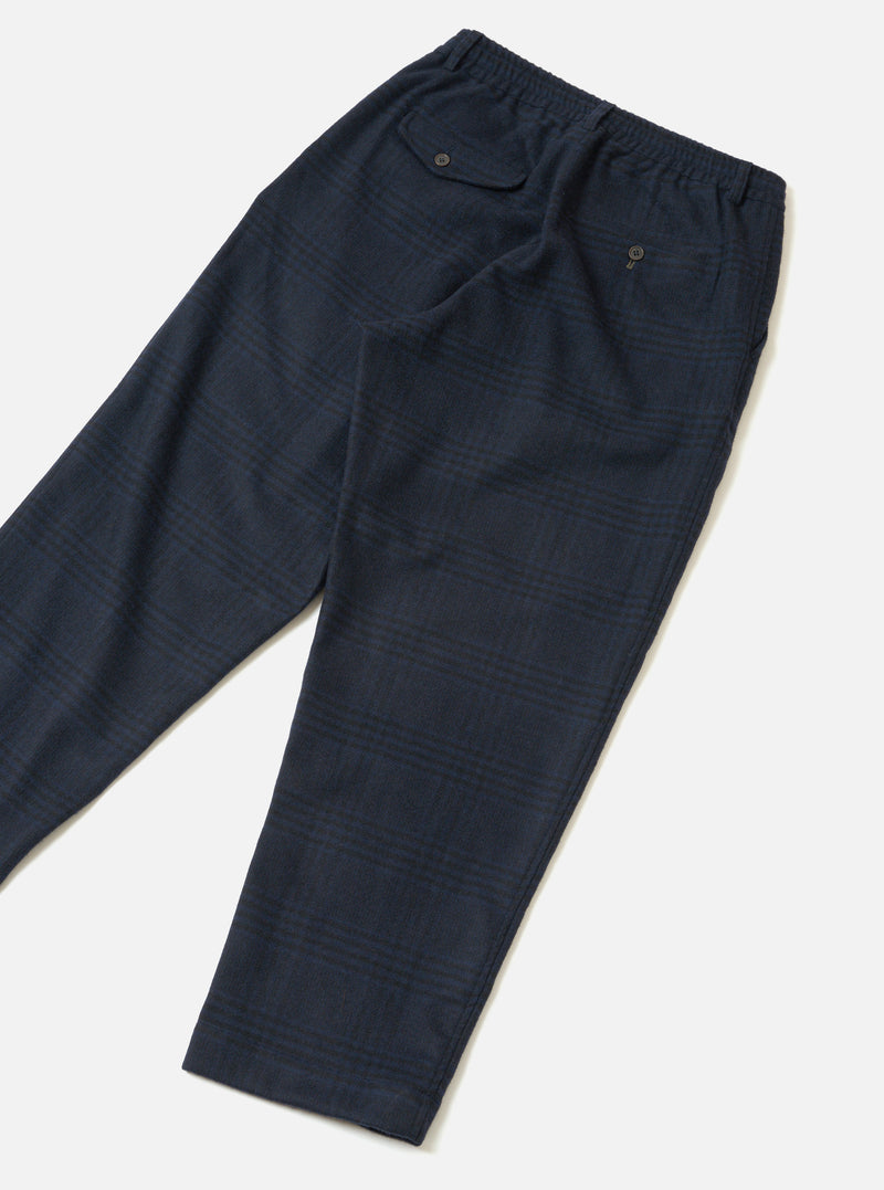 The Navy Bob Wool Mix Oxford Pant is laid flat on a light grey surface. Highlights include a subtle navy and dark green glen check, an elasticated waistband, a buttoned hip flap pocket, a buttoned rear welt pocket, and tapered legs with plain hems.