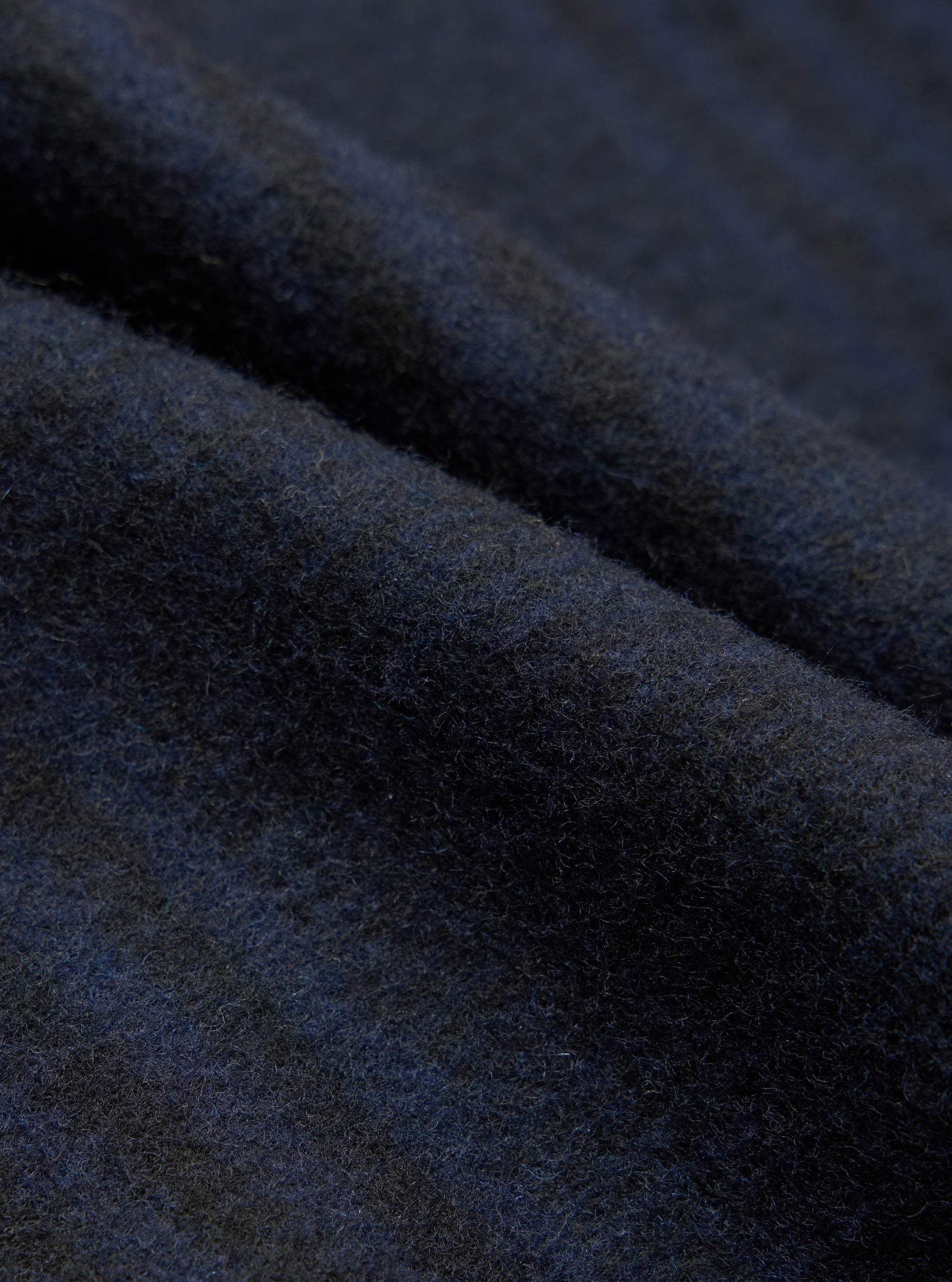 Close-up fabric detail shot of the navy wool mix oxford pant. The brushed, lightly felted textile shows a dense, softly napped surface with fine individual fibres visible throughout. Deep navy tones shift subtly across the folded cloth, revealing slight blue and charcoal variation in the weave.