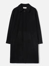 Black wool-look mac coat laid flat on a light grey studio backdrop. Features a point collar, concealed fly-front fastening with a single visible dark button at the neck, two patch pockets at the hip, and long plain sleeves. A Universal Works woven label is visible at the collar.