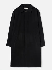 Black wool-look mac coat laid flat on a light grey studio backdrop. Features a point collar, concealed fly-front fastening with a single visible dark button at the neck, two patch pockets at the hip, and long plain sleeves. A Universal Works woven label is visible at the collar.