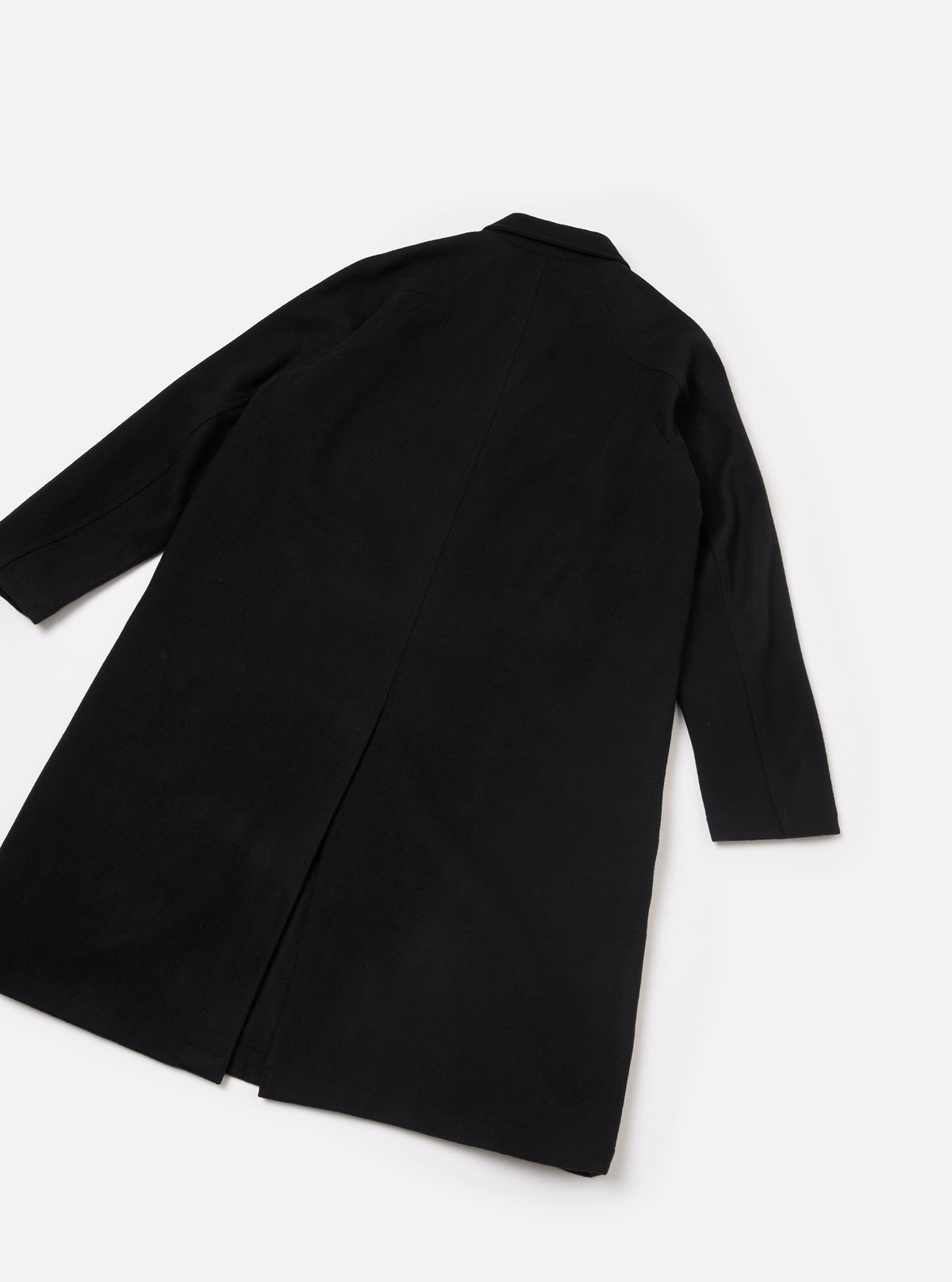 Black Mowbray Mac Coat laid flat on a light grey surface, shot from above at an angle showing the back. The smooth, matte fabric has a clean, unbroken back panel with a centre vent at the hem. A notched collar is visible at the top. Long sleeves with plain cuffs extend to the sides.