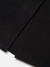 Close-up flat lay of the black Mowbray Mac Coat on a white surface, showing the lower hem and back vent detail. The black wool-blend fabric has a dense, lightly felted texture. The vent is stitched at the base with a clean, structured finish.