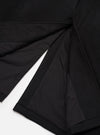 Close-up flat lay of the black Mowbray Mac Coat on a white surface, showing the open back vent detail. The matte wool-blend outer fabric contrasts with the smooth black satin lining visible inside the vent. Topstitched seams and a neatly finished hem are visible at the base of the coat.