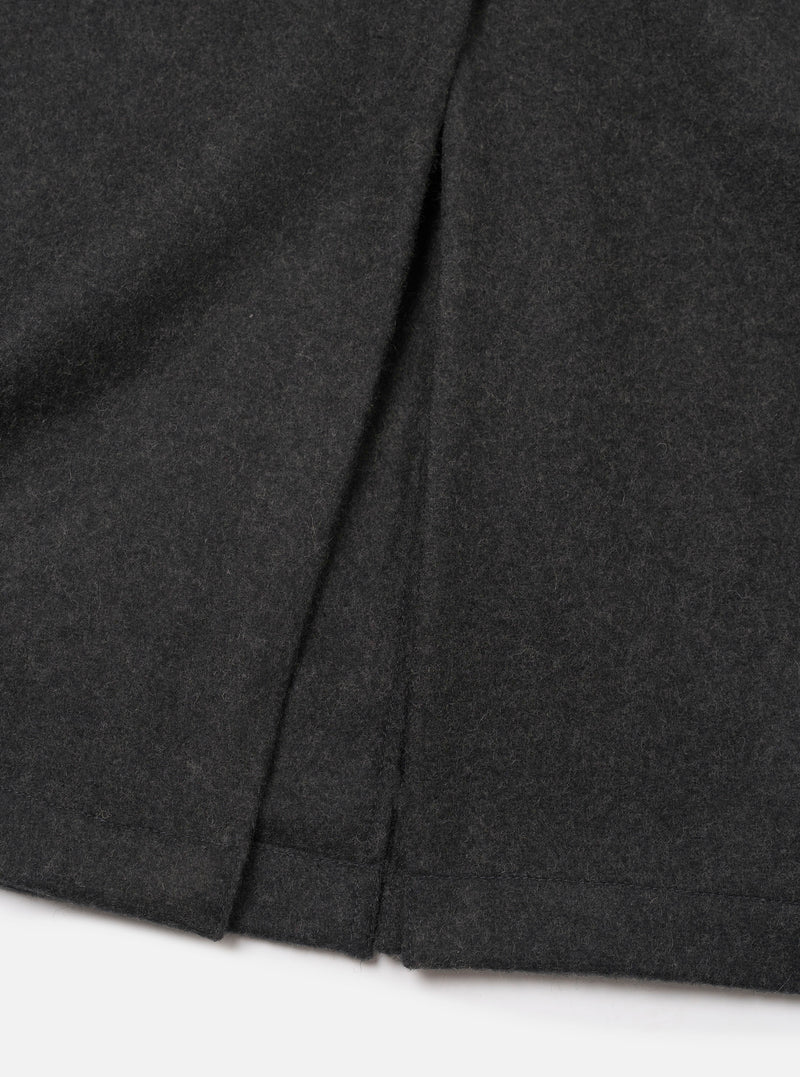 Close-up of the back hem and centre vent of a grey marl wool mac coat, laid flat on a white surface. The mélange fabric has a soft, lightly textured finish. The vent opening and neat hem are clearly visible, showing clean topstitching and precise construction.